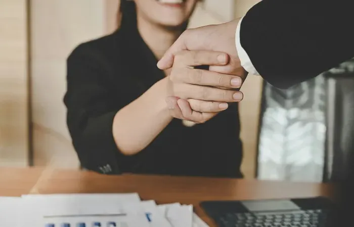 Smiling professional shaking hands across a desk with documents and calculator, illustrating local business